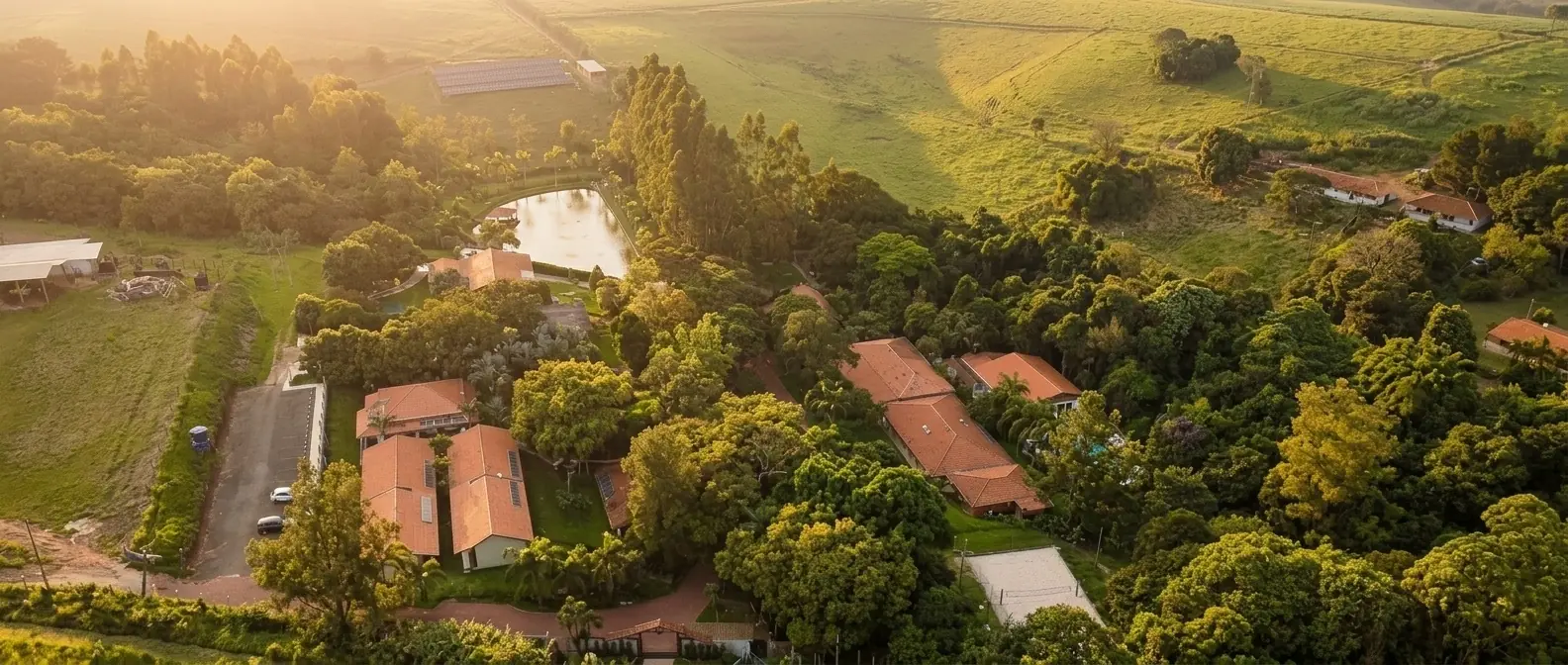 Vista aérea do Água Santa: telhados entre as copas das árvores, lago e mata em Descalvado